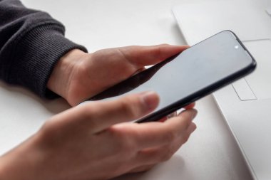 Avrupalı çocuk elleri siyah akıllı telefonu parmakları ve siyah ekranı beyaz masanın üzerinde tutuyor. Okuldaki araştırma ve mobil oyun için beyaz defterin önünde. Ya da çocukların ve yetişkinlerin oyun bağımlılığı için.