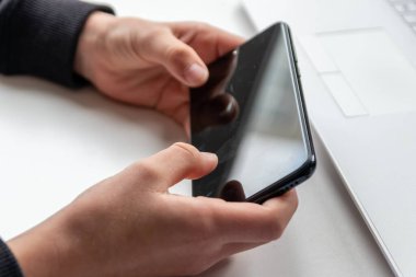 Avrupalı çocuk elleri siyah akıllı telefonu parmakları ve siyah ekranı beyaz masanın üzerinde tutuyor. Okuldaki araştırma ve mobil oyun için beyaz defterin önünde. Ya da çocukların ve yetişkinlerin oyun bağımlılığı için.