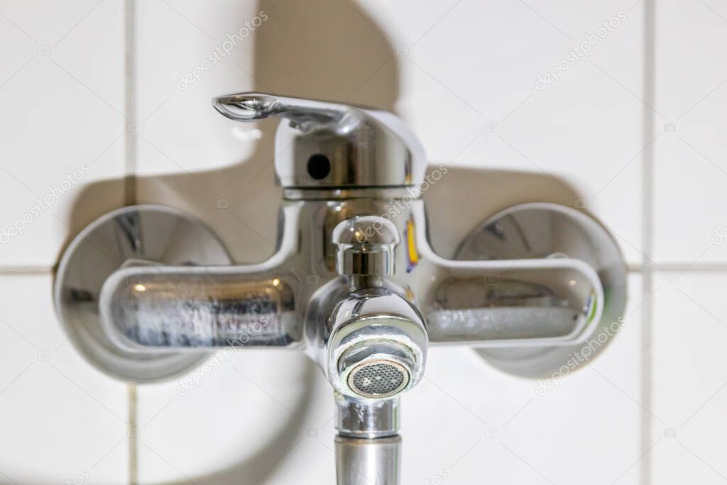 Old fossil bathroom fittings and fossil sanitary with stainless chromed equipment in the restroom for showering or faucet sink shows repair maintenance due to dripping water on chrome wrench