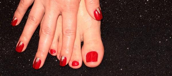 Red pedicure and manicure. A woman\'s leg and arm on a black background.