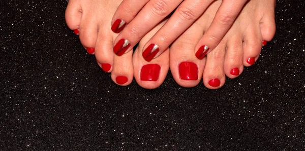 Red pedicure and manicure. A woman\'s leg and arm on a black background.
