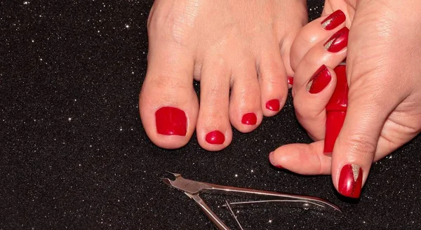 Red pedicure and manicure. A woman\'s leg and hand with a jar of nail Polish on a black background