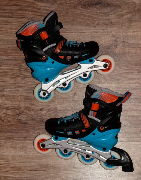 Roller skates on a wooden background. Roller skates are black and blue with orange color.