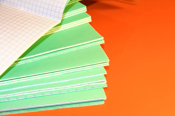 A stack of school green notebooks on a bright background.