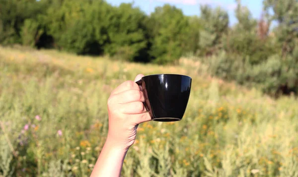 Black Cup in hand against the background of nature. Good morning