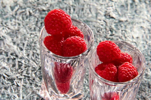 Ripe raspberries in a crystal bowl on a crumpled background.