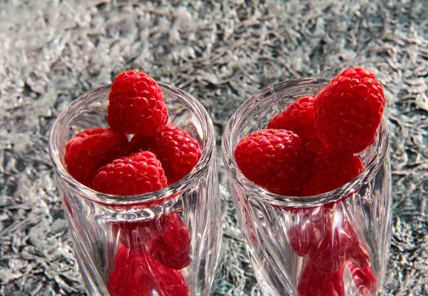 Ripe raspberries in a crystal bowl on a crumpled background.