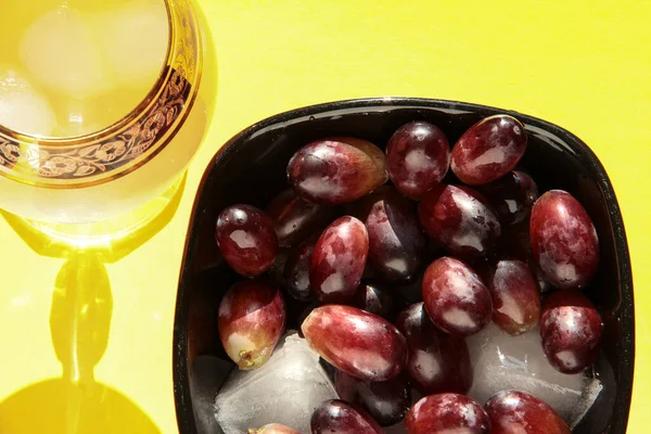 Grapes in a crystal bowl with an icy drink on a bright background.