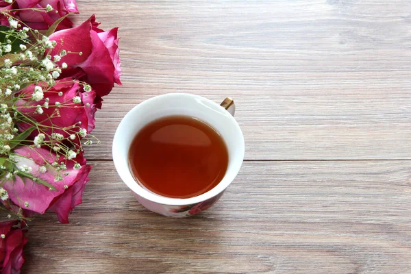 A Cup of tea with roses on a wooden background.