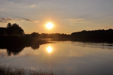 Parlak ve renkli gün batımı Nehri üzerinde. Güneş ağaçların arkasında akşam gizler. Su üzerinde batan güneşin parlamasını