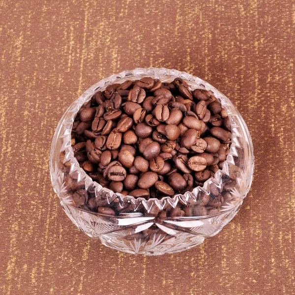 Grains de café torréfiés dans des plats en cristal sur fond brun . — Photo