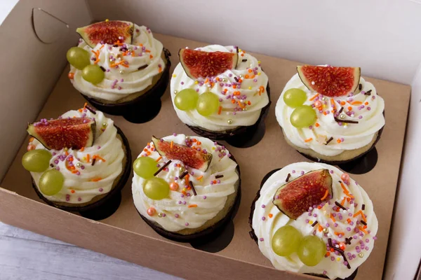 Delicious cupcakes with vanilla cream, figs and grapes in a box for cakes.