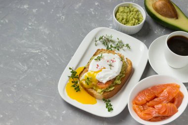 Kahvaltıda sandviç. Somon füme yumurta, kızarmış ekmek, avokado ve beyaz tabakta kahve.