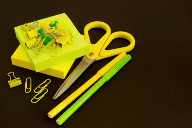 Kırtasiye sarı ve yeşil renkli. Kağıt, keçeli kalem, ataç, siyah arka planda makas. Metin için boşluk.