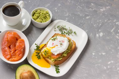  Somon füme yumurta, kızarmış ekmek, avokado ve beyaz tabakta kahve. Kahvaltıda sandviç..