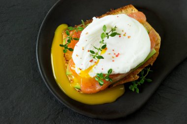 Somon füme yumurta, kızarmış ekmek, avokado ve siyah tabakta kahve. Kahvaltıda sandviç..