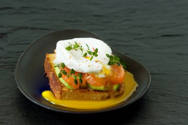 Somon füme yumurta, kızarmış ekmek, avokado ve siyah tabakta kahve. Kahvaltıda sandviç..