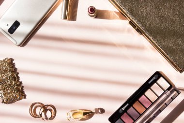 Pembe arka planda bir takım kozmetik ve aksesuarlar. Güneş ışığı ve sert gölgeler.