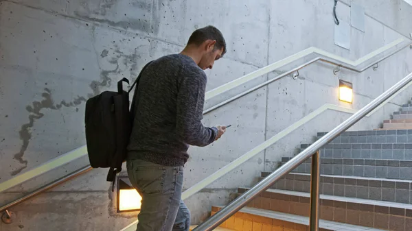 Genç adam istasyonda merdivenlerden çıkıyor ve elinde bir telefon ve sırtında bir sırt çantası tutuyor. Trende, otobüste, metroda, istasyonda aceleyle giden bir adam..