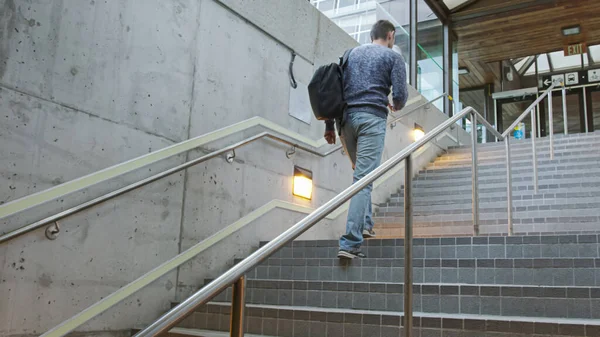 Young man climbs the stairs at the station and holds a phone in his hands and a backpack on his back. A man hurries on a train, bus, airplane subway, transport on a station.