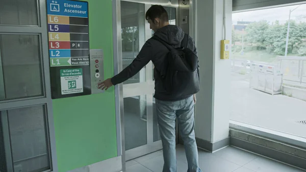 年轻人在停车场或车站等电梯 穿着休闲装和背包的男人点击电梯按钮 进入电梯门 免版税图库图片