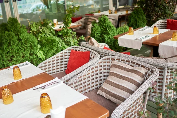 Summer terrace veranda of the cafe. Cozy gray wicker chairs with cushions, served tables and green bushes — Stock Photo, Image