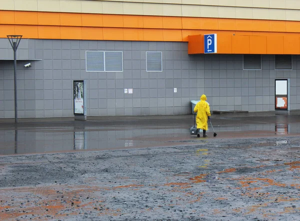 穿着黄色雨衣的看门人在雨中倒垃圾 免版税图库图片