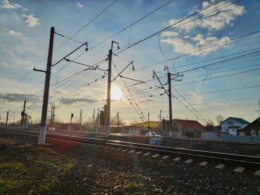 Demiryolu rayları ile kırsal fotoğraf, bulutlar ve batan güneş ile bahar gökyüzünün arka plan karşı elektrik sütunları