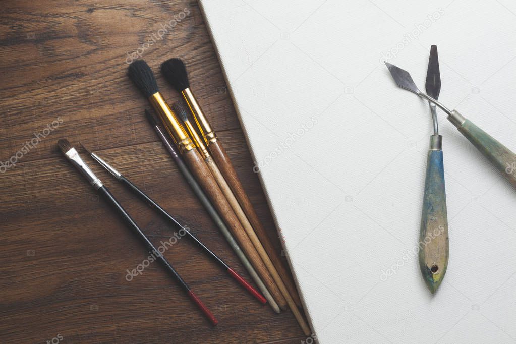 paint brushes and blank canvas over wooden background