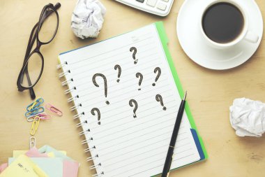 Soru işaretleri üstünde beyaz bir defter hesap makinesi ve gözlük ile yazılı