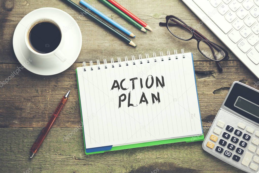 action plan text on notebook with keyboard and stationary on table