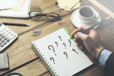 adam soru işaretleri defter sayfası ile sabit ve ahşap masa kahve yazmıştır