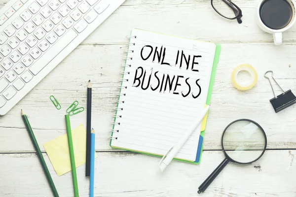 online business text on notepad with pencils, computer keyboard, eyeglasses and coffee cup on white wooden table