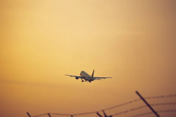 Silhouette of plane and fence on orange sky at sunset