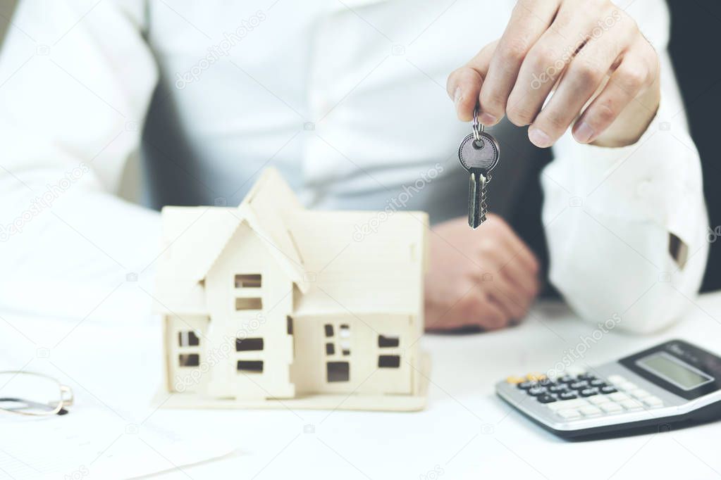 male hands holding key over table with house model 