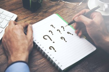 adam notepad ile masa üstünde klavye üzerinde soru işaretleri yazmıştır