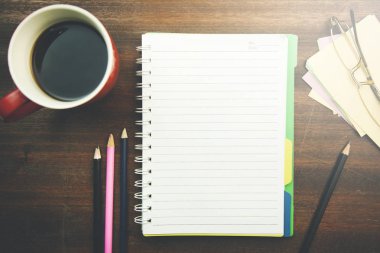 Ahşap masa üzerinde ofis malzemeleri ve kahve fincanı ile boş not defteri.