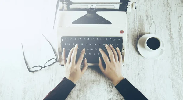 Hands writing on typewriter with coffee and glasses on table