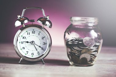 Masadaki kavanozda bozuk para olan saat.