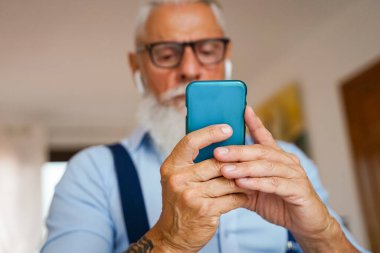 Evde çekici bir adam var, akıllı telefonda şarkılarını ve şarkılarını değiştiriyor, kablosuz kulaklıkla müzik dinliyor. Sakallı adam. odaklanma elleri - Resim