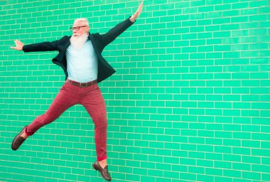 Çılgın adam zıplıyor. Mutlu erkek kutlaması. Enerjik, mutlu, sıradan kıyafetlerle atlayan olgun bir adam, açık yeşil arka planda izole edilmiş bir duvar - neşeli yaşlı yaşam tarzı konsepti - yüze odaklan.