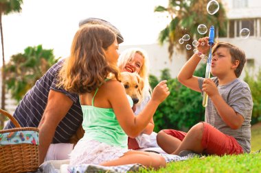 Anne, baba, oğul ve köpekleri mutlu bir yaz zamanı gülüyor, çocuk sabun köpüğüyle oynuyor. Mutlu aile parkta piknik yapıyor. Çocuğa odaklan - Görüntü