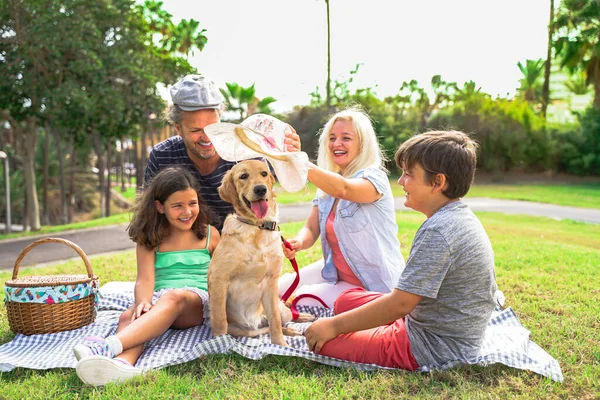 Family playing with the dog. beautiful day in the park. Happy family doing picnic in the nature outdoor. Focus the dog - Image