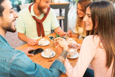 Barda kahvaltı yapan çiftler var. Romantik bir randevuda aşıklar. Genç çiftler el ele tutuşup seramik bardaklarda cappuccino içerler. Ellere odaklan..