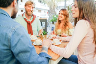 Barda kahvaltı yapan çiftler var. Romantik bir randevuda aşıklar. Genç çiftler el ele tutuşup seramik bardaklarda cappuccino içerler. Ellere odaklan..