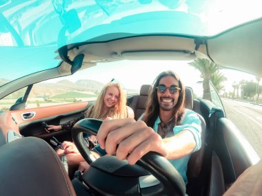 Mutlu genç çift üstü açık arabayla yolculuk ederken eğleniyor. Romantik aşıklar tropik bir şehirde lüks bir tatilde Cabriolet araba sürerek eğleniyorlar. Tatil, yolculuk ve ilişki konsepti - Görüntü