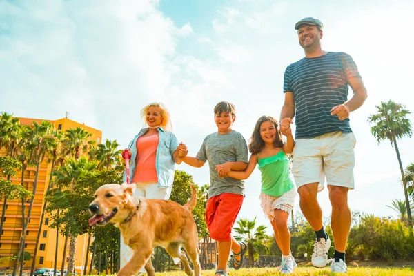 Baharda parkta iki çocuklu ve köpekli bir aile. Mutlu aile çimlerin üzerinde birlikte koşuyor - Görüntü
