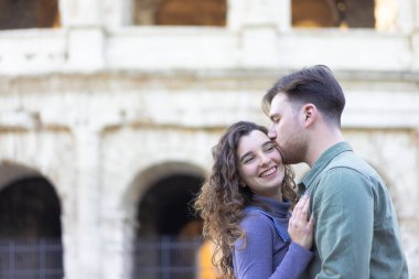Coliseum 'un güneşli bir gününde eğlenen, tatlı bir çift öpüşüyor. Ünlü anıtları ziyaret eden mutlu turistler. Balayı gezisi, turizm, aşk tatili ve tatil gezisi konsepti.