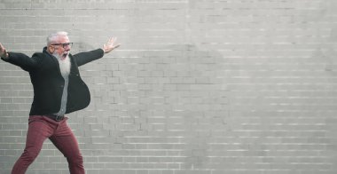 Çılgın adam zıplıyor. Mutlu erkek kutlaması. Enerjik, mutlu, günlük kıyafetlerle zıplayan olgun bir adam, açık gri arka planda izole edilmiş bir duvar - neşeli, yaşlı yaşam tarzı konsepti - görüntü