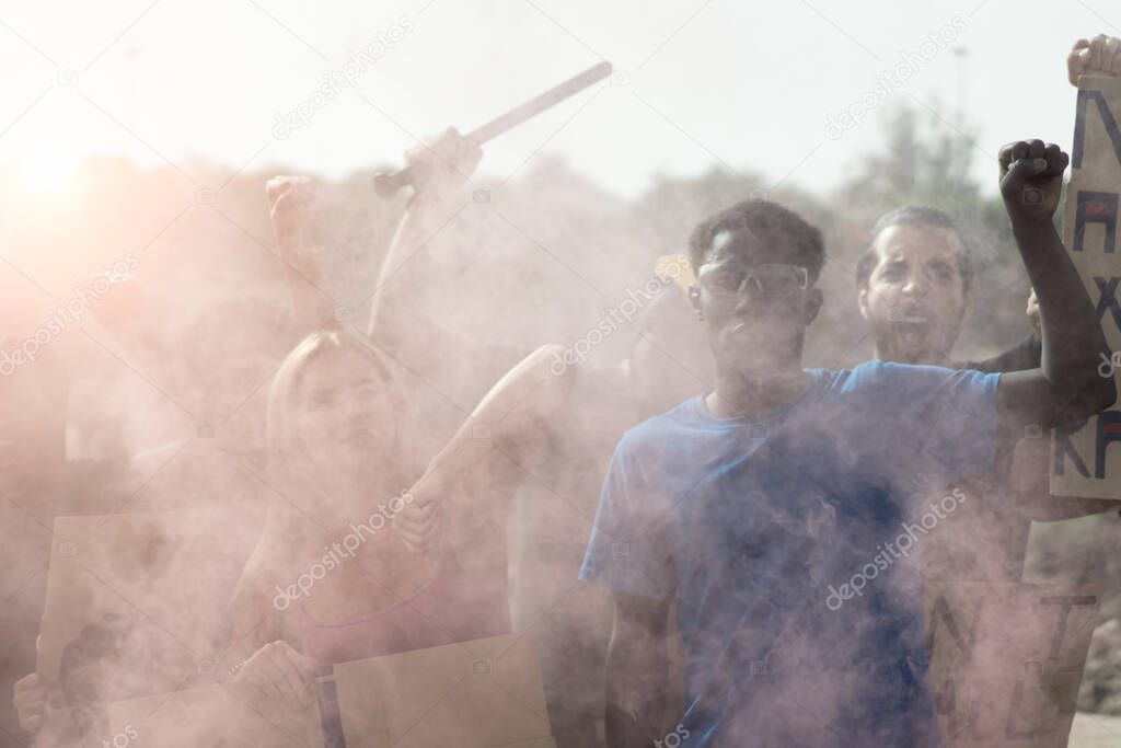 Small activist group going against police throwing tear gas. Multiethnic people fighting for human rights. Black lives matter and no racism concept. Defocused image for the smoke.